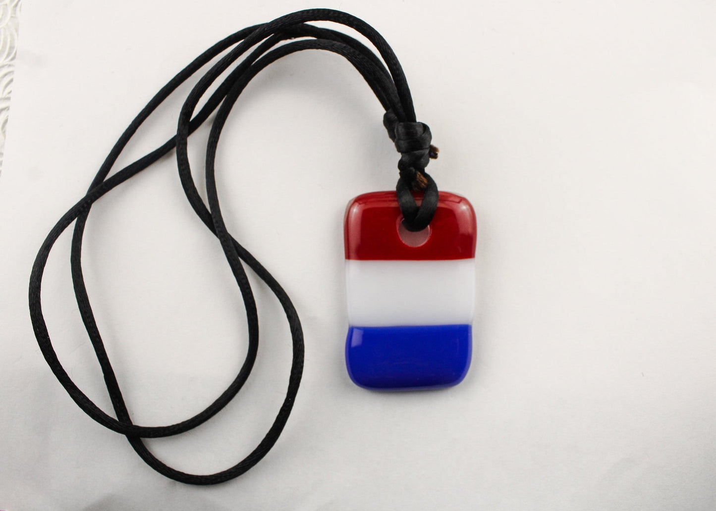 Red, white, and blue striped pendant on a black cord against a white background